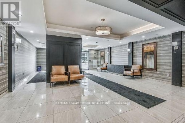 Luxury apartment building lobby with tiled floors, leather chairs, and decorative wall panels. - 514 - 125 Shoreview Place, Hamilton