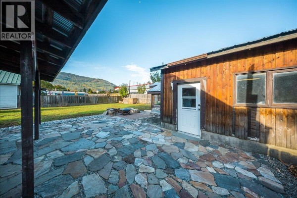 Rear of a wooden building with a door and windows on a flagstone patio. - 514 Davies Avenue, Salmo