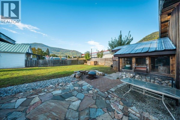 Outdoor space with a flagstone patio, fire pit, and grassy yard with mountains beyond. - 514 Davies Avenue, Salmo