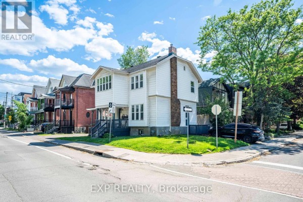 Corner view of a white multi-family house with a large brick chimney and surrounding residential buildings. - 514 Lyon Street N, Ottawa