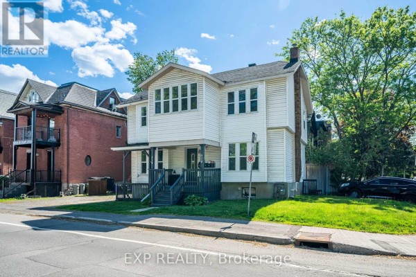 Three-quarter exterior view of a white vinyl-sided multi-family home with a porch and residential buildings nearby. - 514 Lyon Street N, Ottawa