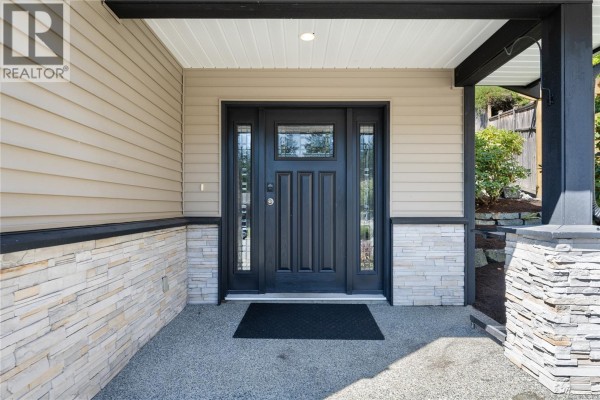 Exterior view of a dark wood front door with glass panes, beige siding, and stone accents. - 5141 Owlstone Pl, Nanaimo