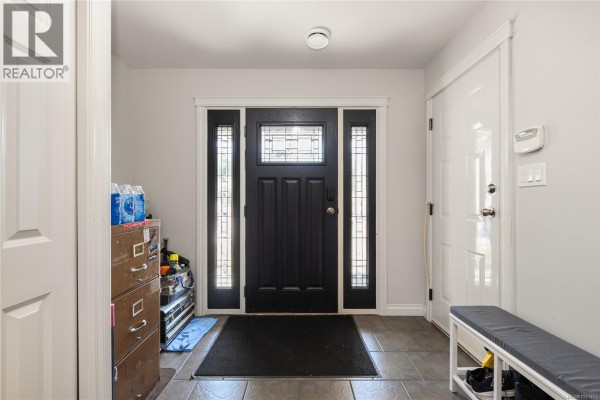 Interior view of a dark wood front door with glass panels, grey tiled floor, and storage furniture. - 5141 Owlstone Pl, Nanaimo