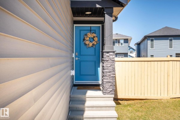 Close-up of a blue front door with a wreath and stone accents on a light-colored siding house. - 5142 23a Av Sw, Edmonton