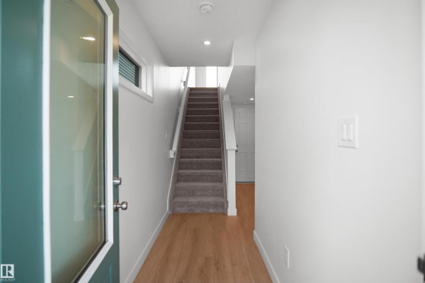 Open hallway with stairs, large window, and light wood flooring - 5145 River's Edge Wy Nw, Edmonton