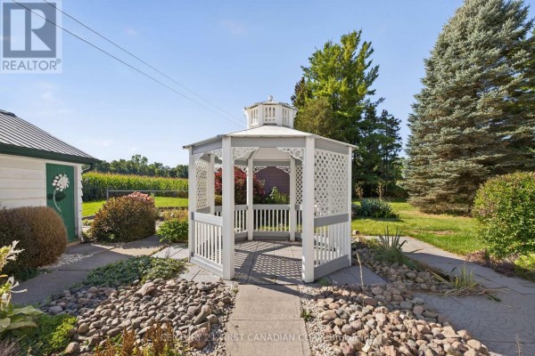 White and gray gazebo in a yard with landscaping and a cornfield - 5147 Egremont Drive Middlesex Centre