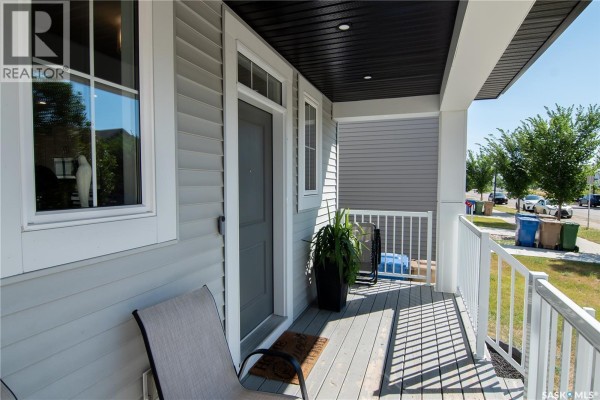 Covered front porch with gray floorboards, white railing, and seating. - 5148 Buckingham Drive E, Regina