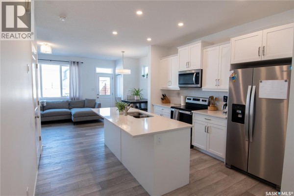 Open-concept kitchen with white cabinets, stainless steel appliances, and island. - 5148 Buckingham Drive E, Regina