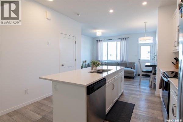 View from kitchen island to living area with gray sectional sofa. - 5148 Buckingham Drive E, Regina