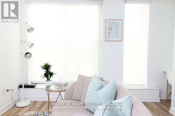 A light-filled living area with a curved sofa, aqua cushions, and large windows. - 515 - 106 Dovercourt Road, Toronto