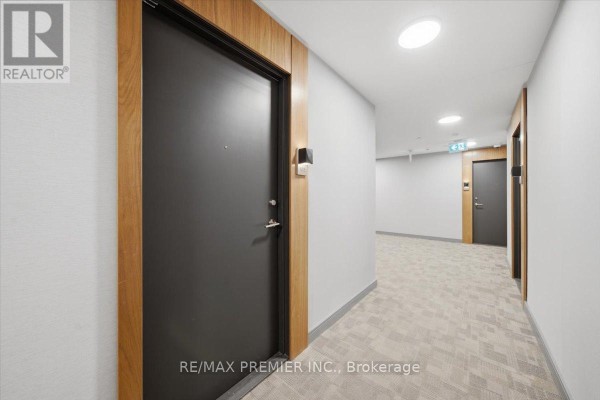 Apartment building hallway with gray carpet, white walls, and dark apartment doors. - 515 - 25 Neighbourhood Lane, Toronto