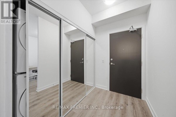 Apartment entryway with gray wood-look flooring, white walls, and mirrored closet doors. - 515 - 25 Neighbourhood Lane, Toronto