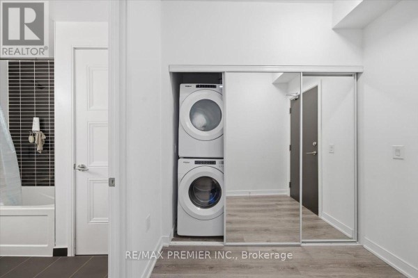 Apartment hallway with stacked white washer and dryer behind mirrored closet doors. - 515 - 25 Neighbourhood Lane, Toronto