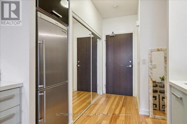 Hallway with stainless steel refrigerator, mirrored closet doors, hardwood floors, and two interior doors - 515 - 38 Dan Leckie Way Toronto