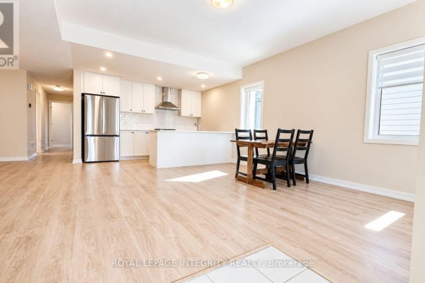 Living area with light wood floors, white kitchen, stainless steel refrigerator, and white cabinetry. - 515 Celestine Private, Ottawa