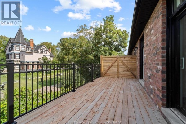 Wooden deck with black metal railing and view of historic building and trees. - 515 Dalhousie Street Unit# 2b, Amherstburg