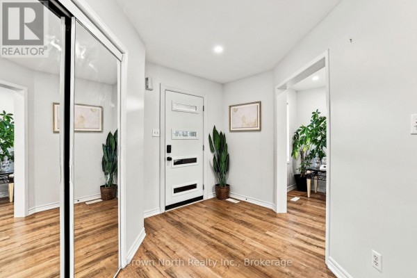 Interior view of the foyer showcasing a white door, hardwood floors, and large mirrored closet. - 515 Ormond Drive, Oshawa