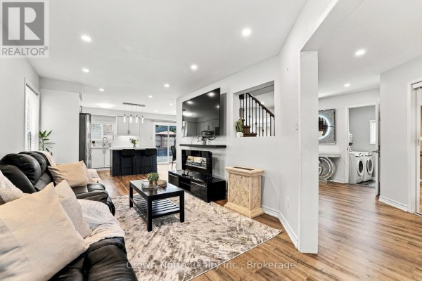 Living room with a black leather sofa, patterned rug, and view into the kitchen and laundry area. - 515 Ormond Drive, Oshawa
