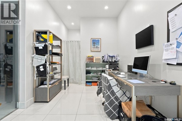 Home office with a gray desk, computer, shelving units, and a light gray wall. - 515 Pohorecky Lane, Saskatoon