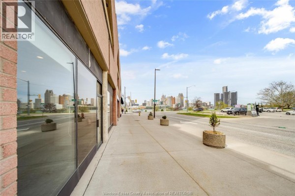 Exterior view of a commercial building with large glass windows reflecting a city skyline. - 515 Riverside Drive West Unit# 104 A, Windsor