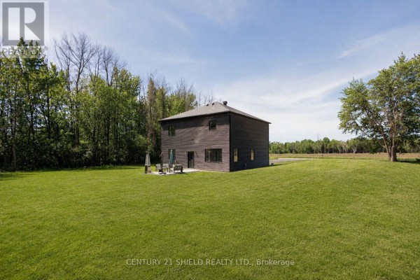 Rear view of the modern home showing a backyard with a patio and green lawn. - 5153 Archer Road, South Dundas