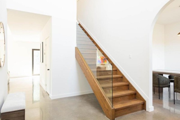Interior view of a bright hallway with a wooden staircase featuring glass railings and concrete floors. - 5153 Archer Road, South Dundas