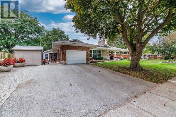 Driveway leading to the attached garage of a brick house, with mature trees on the property. - 5159 Shirley Avenue, Niagara Falls