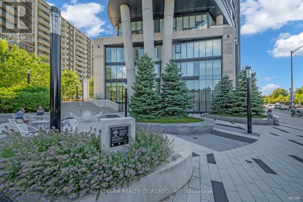Outdoor seating area with modern white chairs and tables next to a condo entrance. - 516 - 585 Bloor Street E, Toronto