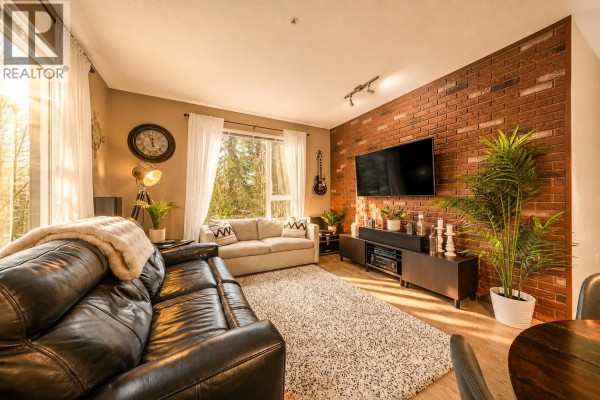 Another angle of the living room showcasing a brick accent wall and entertainment unit. - 516 9250 University High Street, Burnaby