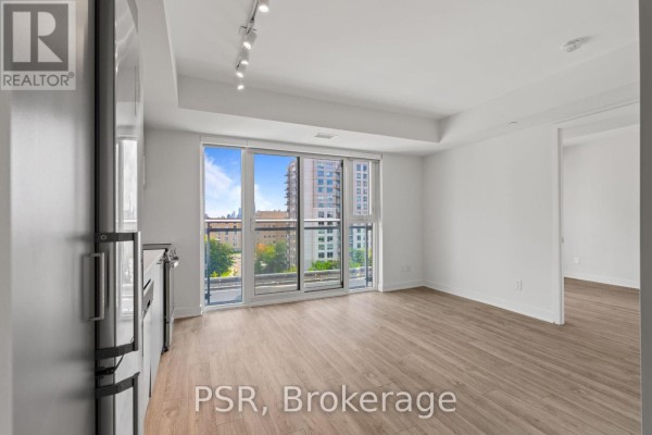 Living area with light wood floors, white walls, and a large glass door opening to a balcony with city views. - 517 - 299 Campbell Avenue, Toronto