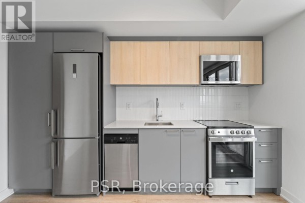Close-up of the kitchen area showing grey cabinets, stainless steel refrigerator, dishwasher, oven, and light wood upper cabinets. - 517 - 299 Campbell Avenue, Toronto