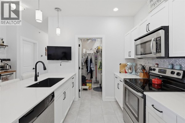 White kitchen with stainless steel appliances, quartz countertops, and tile backsplash. - 5170 Dallas Drive Unit# 512, Kamloops