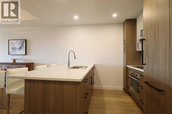 Kitchen with a large island, built-in oven and stovetop, and modern wood and white cabinetry. - 518, 102 Scenic Drive N, Lethbridge