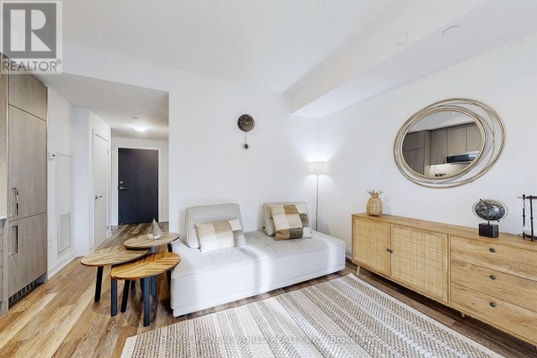 Living space with a sofa, patterned rug, woven sideboard, and an entryway with a dark door. - 518 - 250 Lawrence Avenue W, Toronto