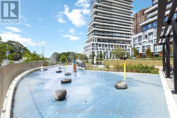 The glass entrance canopy of a modern apartment building with planters and seating. - 518 - 30 Inn On The Park Drive, Toronto