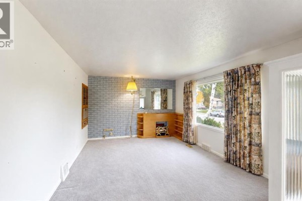 Living room with a grey carpet, white walls, patterned curtains, and a light blue brick fireplace. - 518 11 Street N, Lethbridge