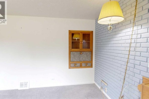 Living room with white walls, light blue brick accent wall, and a wooden built-in cabinet with glass doors. - 518 11 Street N, Lethbridge