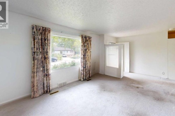 Living room with grey carpet, patterned curtains, a large window overlooking the street, and a glass-paneled door. - 518 11 Street N, Lethbridge