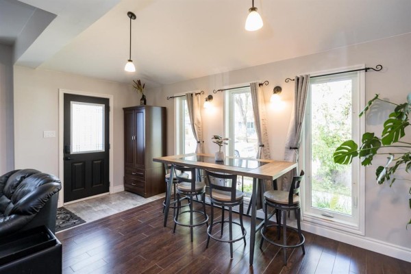 Dining area with a high table, stools, dark wood floor, and black door. - 518 Harvard Avenue E, Winnipeg