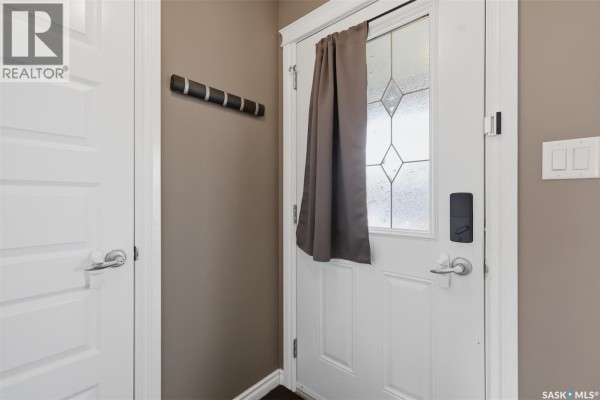 Interior view of a front door with a frosted glass window, a coat rack, and adjacent doors. - 518 Klassen Crescent, Saskatoon