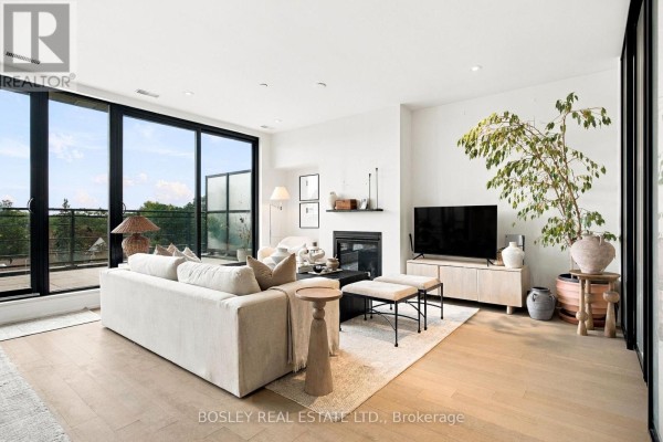 Living room features a fireplace, television, and a large sectional sofa with light wood floors. - 519 - 365 Beech Avenue, Toronto