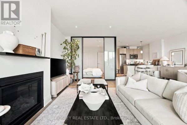 Living area with fireplace, television, and kitchen visible through a sliding glass partition. - 519 - 365 Beech Avenue, Toronto