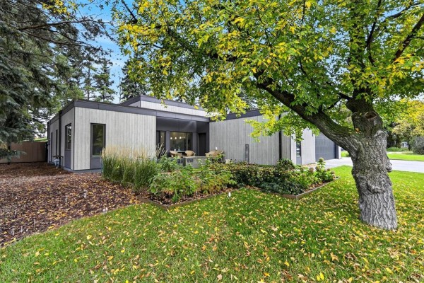 Side view of a modern house with gray siding, garden beds, and a large tree. - 519 Cote Avenue, St Pierre Jolys