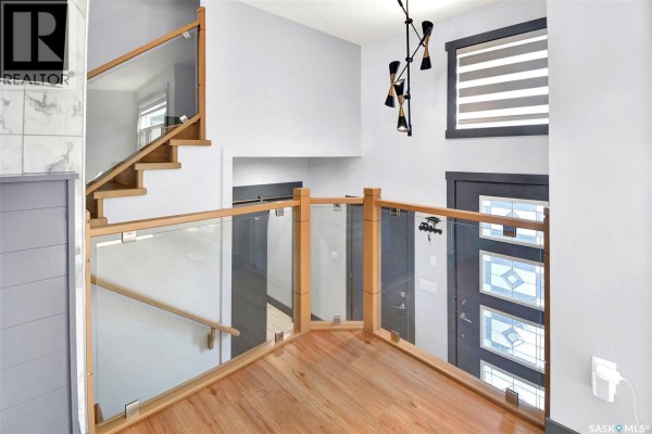 View from the upper landing of a staircase with glass and wood railings overlooking the entrance. - 519 Kenaschuk Way, Saskatoon