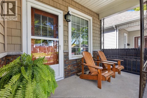 Close-up of the covered porch with two wooden Adirondack chairs and a potted fern. - 519 Mckay, Windsor