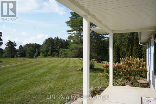 View from a covered porch looking out onto a large, well-maintained lawn with mature trees. - 5194 Bruce Road 3 Road, Saugeen Shores