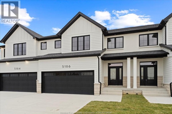 Exterior view of a white townhouse with black trim, black garage doors, and stone accents. - 5194 Talia Trail, Tecumseh