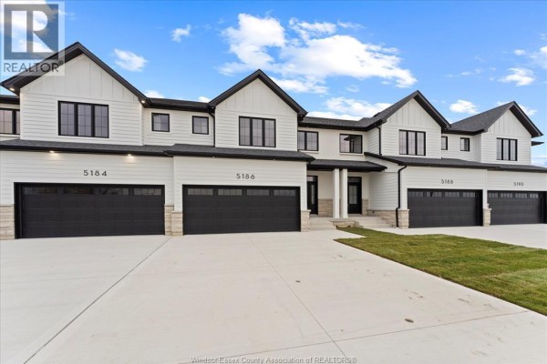 Exterior view of a white townhouse complex with black trim and black garage doors. - 5194 Talia Trail, Tecumseh