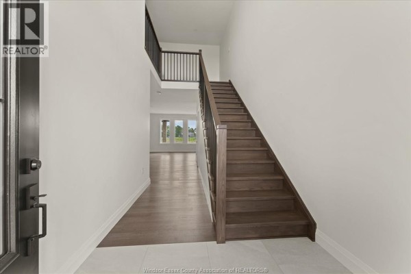 Interior view of a foyer with a wood staircase, dark metal railings, and hardwood floors. - 5194 Talia Trail, Tecumseh