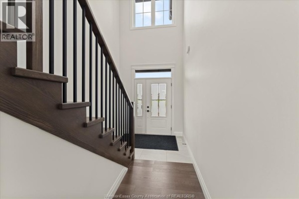 Interior view of a foyer with a white staircase, dark metal railings, and double glass doors. - 5194 Talia Trail, Tecumseh